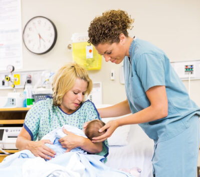 Mid adult nurse helping woman in holding newborn baby at hospital room